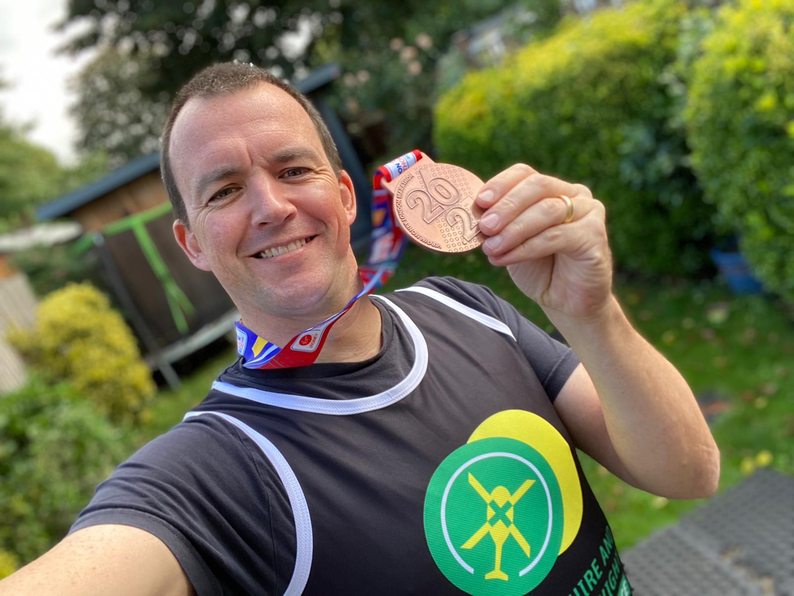 Ed Danson holding his London Marathon medal wearing a HIOWAA running vest