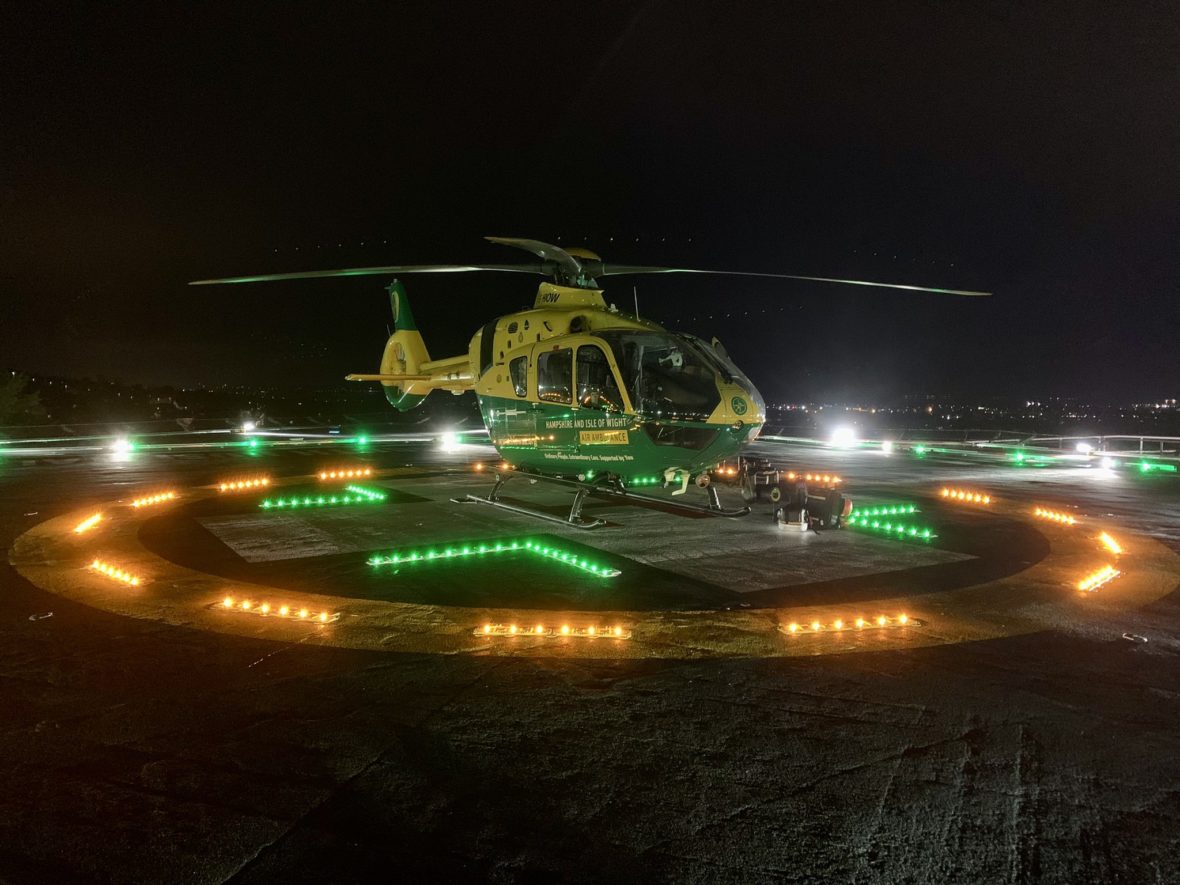 A helicopter on a rooftop helicopter at night surrounded by lights