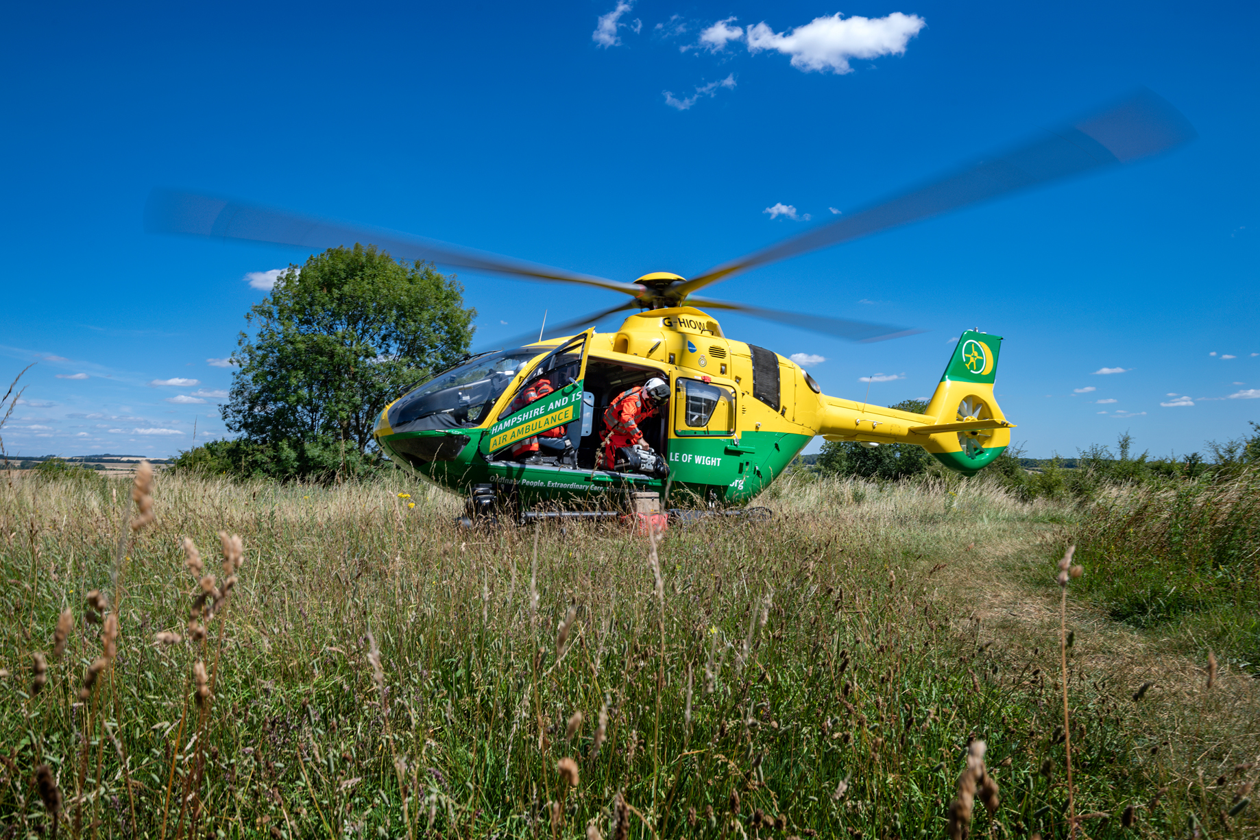 A helicopter has landed on a field. Crew are leaving the helicopter.