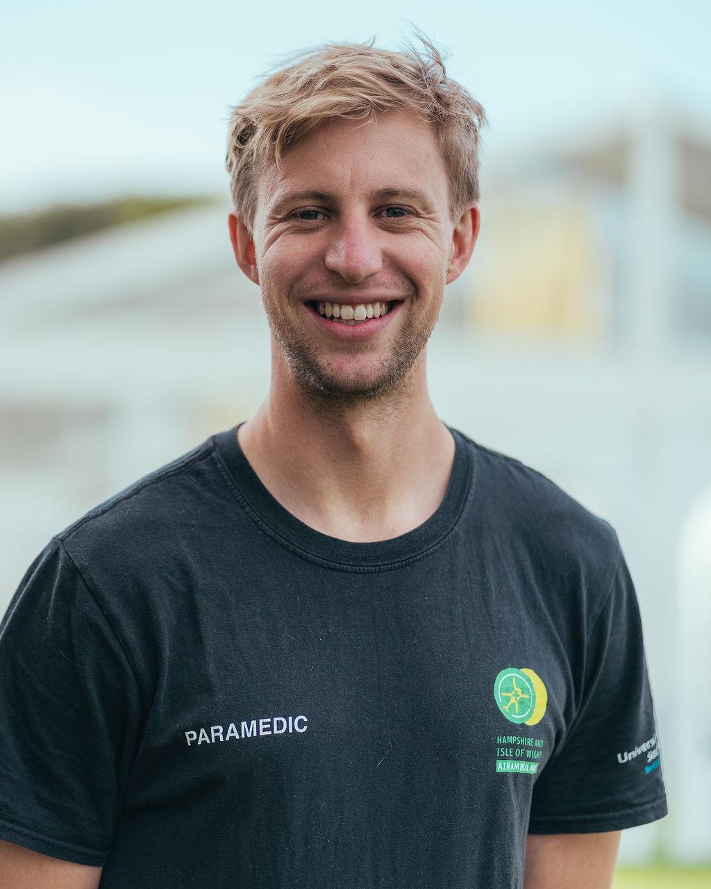 Specialist Paramedic Julian is wearing his black branded top and smiling to camera