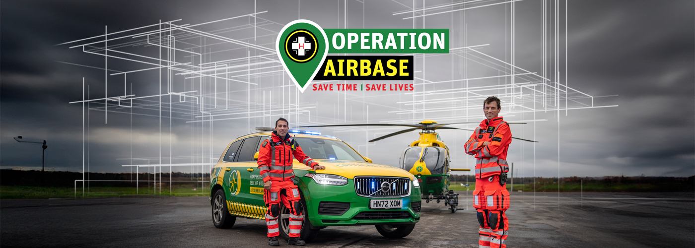 A doctor and paramedic are standing in front of an emergency response vehicle and the helicopter. There is a sketch of a building in the background to symbolise a new hangar. The appeal logo is top centre of the image.