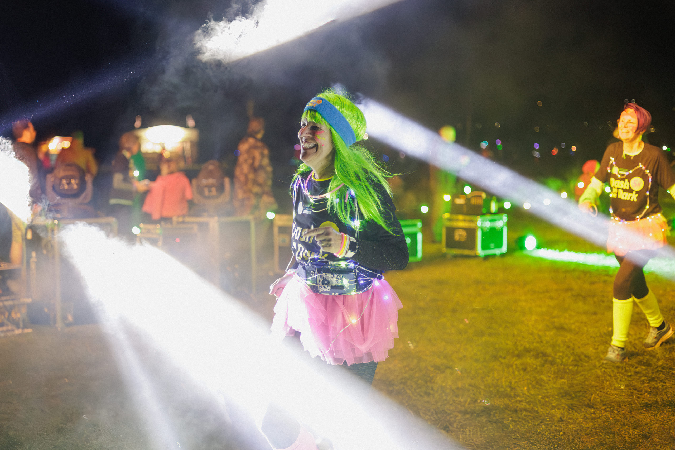 A person wearing a neon headband and tutu through bright spotlights