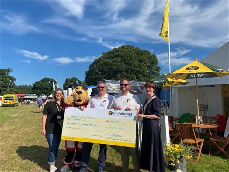 People in a sunny field holding a large cheque.