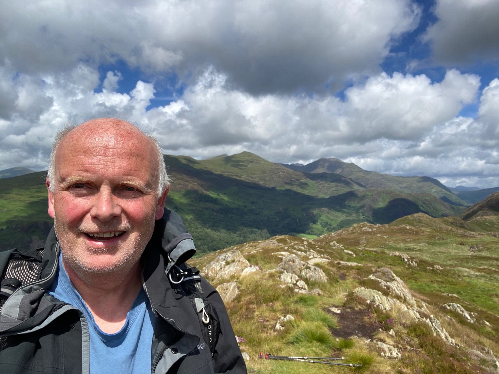 A man standing on a grassy hill. There are a range of hills in the background.