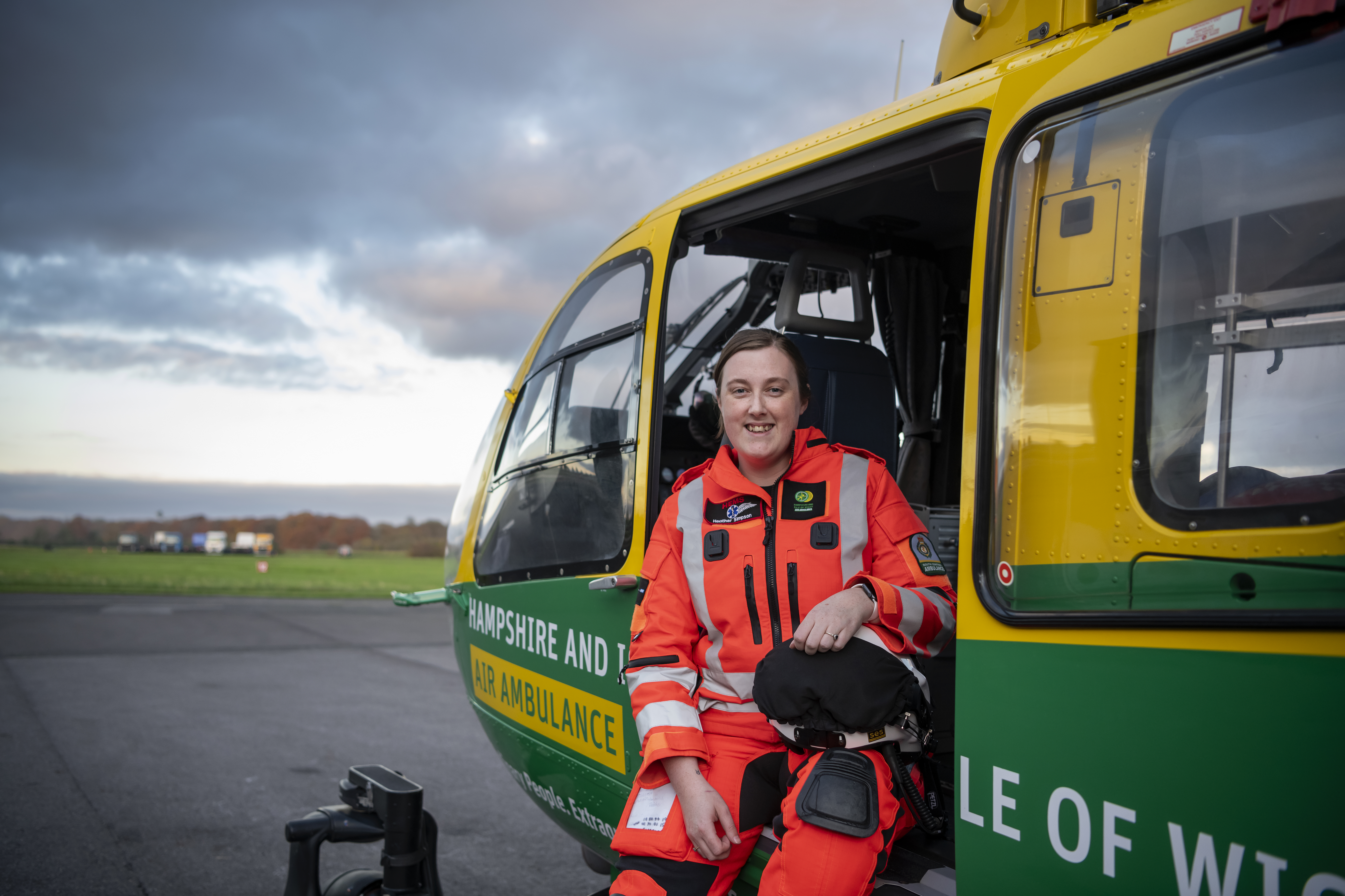 Heather is sitting in the aircraft in full flight suit. She is smiling to the camera and resting her hand on her flight helmet.