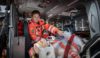 An air ambulance doctor sat in the back of a helicopter with a training manikin that is secured to a stretcher.